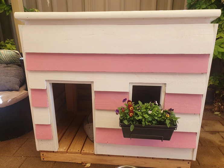 Pink-and-white wooden dog kennel with a flower-filled window box